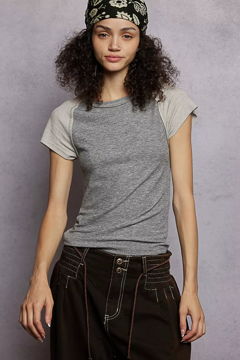Woman wearing a gray t-shirt and dark pants against a gray background