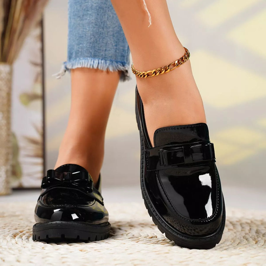 Black glossy loafers worn with denim jeans on a blurred background