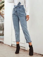 Person wearing blue denim overalls and black boots against a white wall.