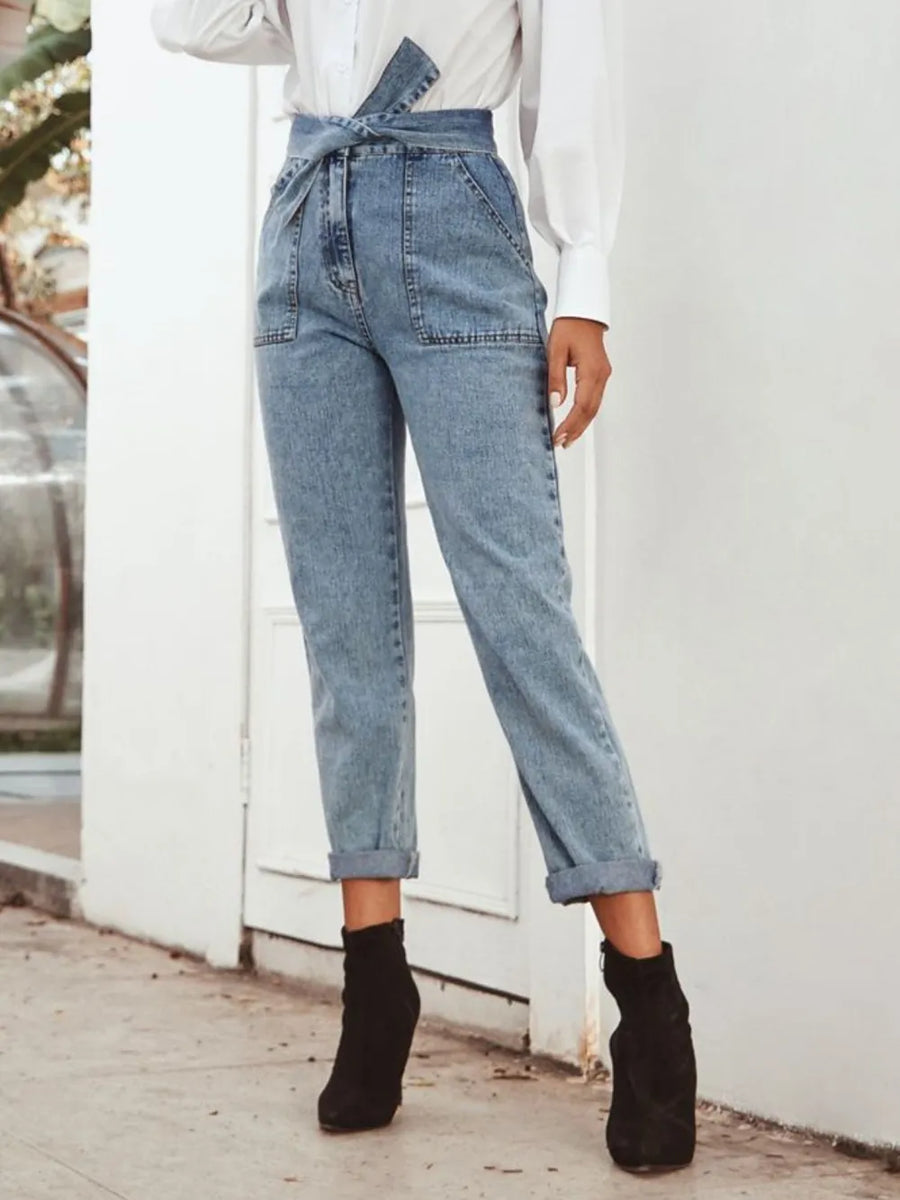 Person wearing blue denim overalls and black boots against a white wall.