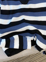 A close-up of a ribbed knit sweater with horizontal stripes in navy blue, medium blue, white, and black, draped on a neutral fabric surface.