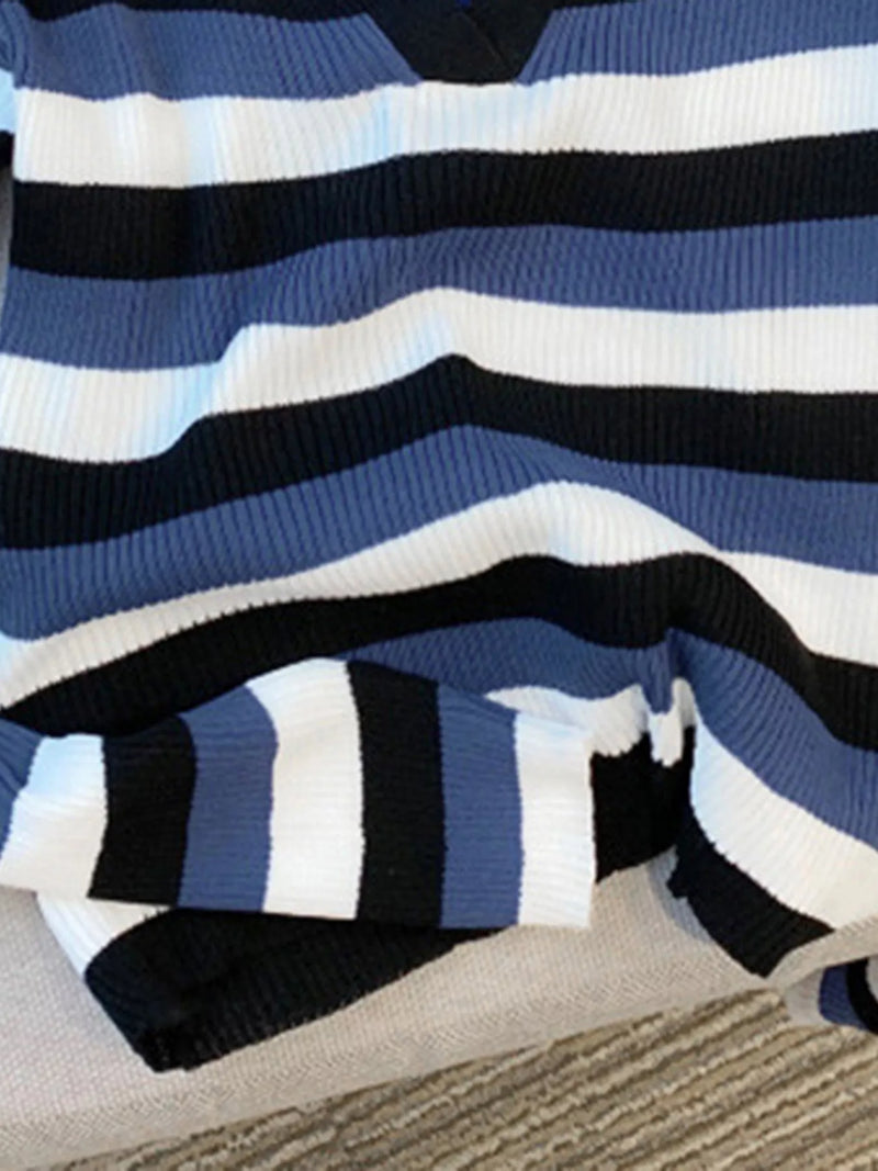A close-up of a ribbed knit sweater with horizontal stripes in navy blue, medium blue, white, and black, draped on a neutral fabric surface.