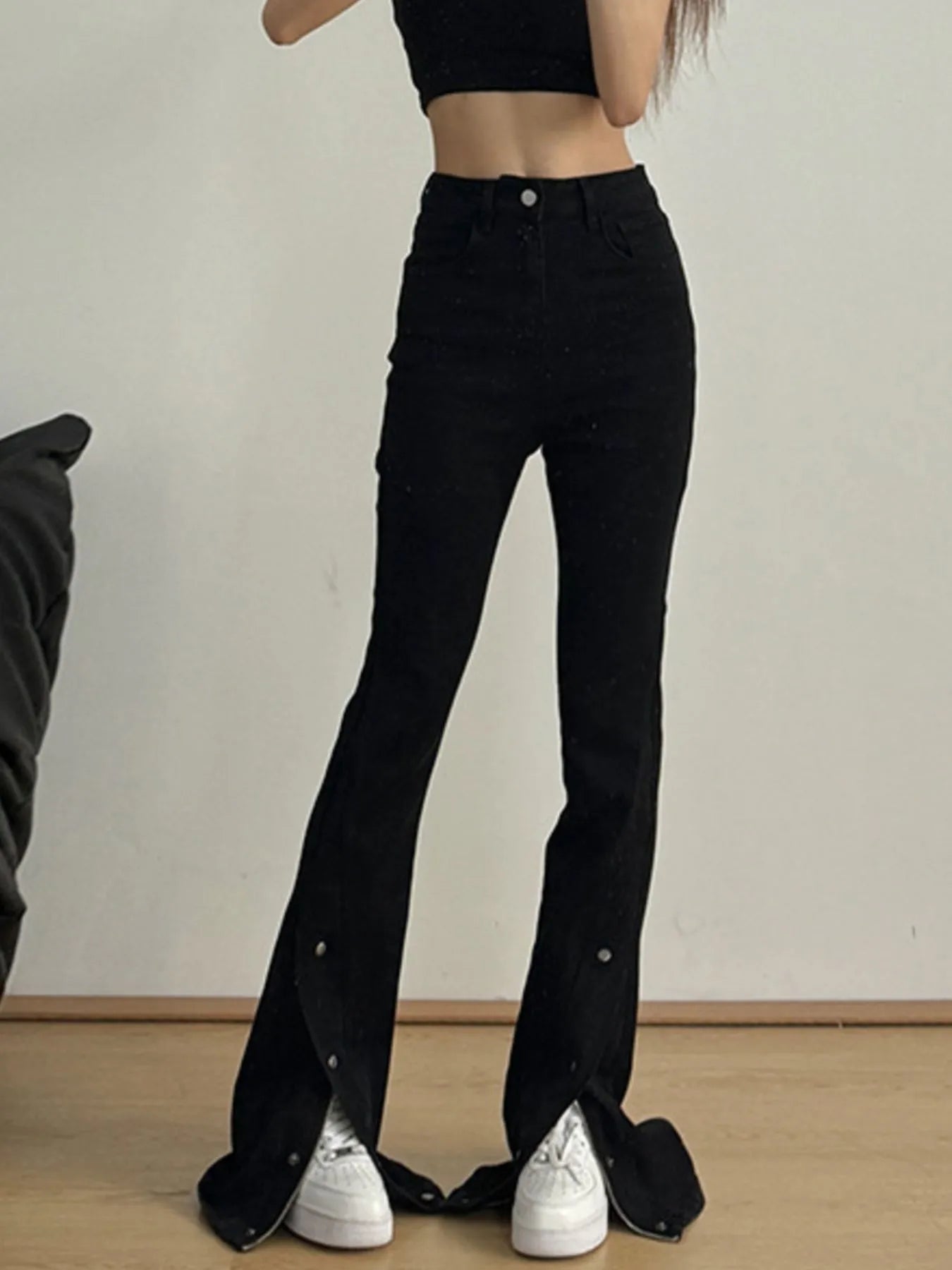 Person wearing black flared jeans and white sneakers on a plain background