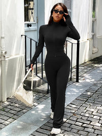 Woman in a black outfit standing on a sidewalk with a white building in the background