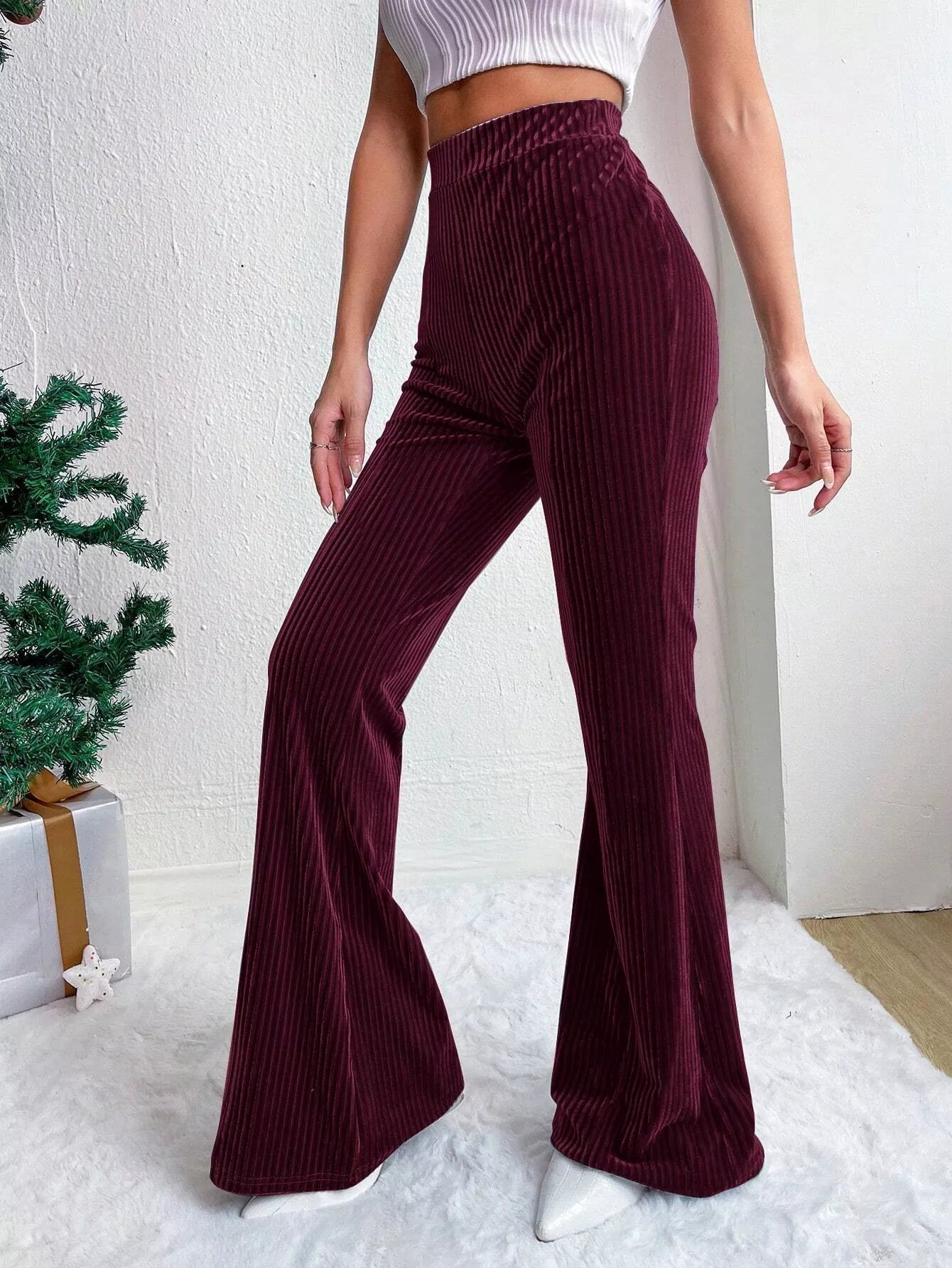 Person wearing burgundy flared pants with a white top against a white wall.