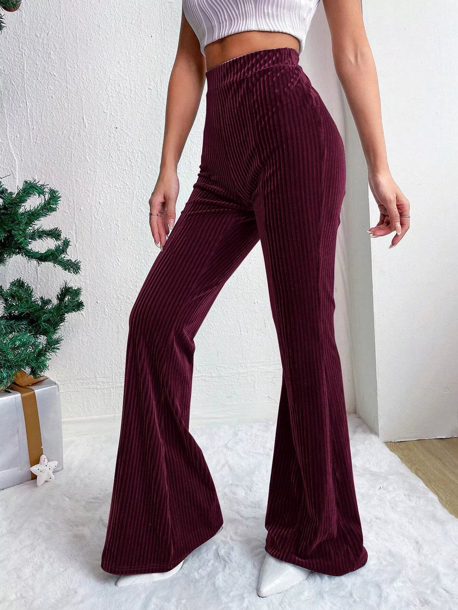 Person wearing burgundy flared pants with a white top against a white wall.