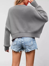 Person wearing a gray sweater and denim shorts on a plain background