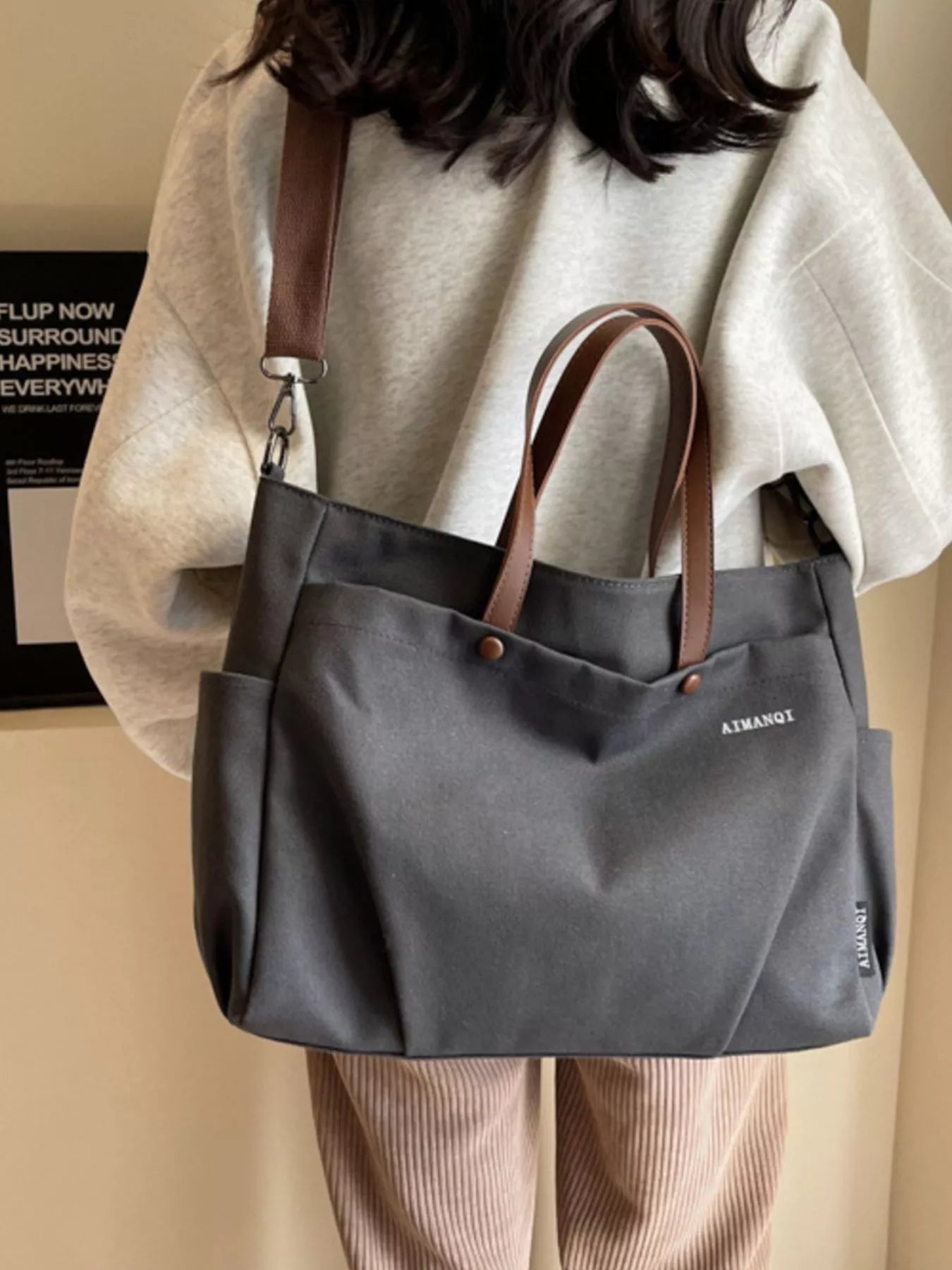 Person wearing a gray tote bag with brown straps on a plain background