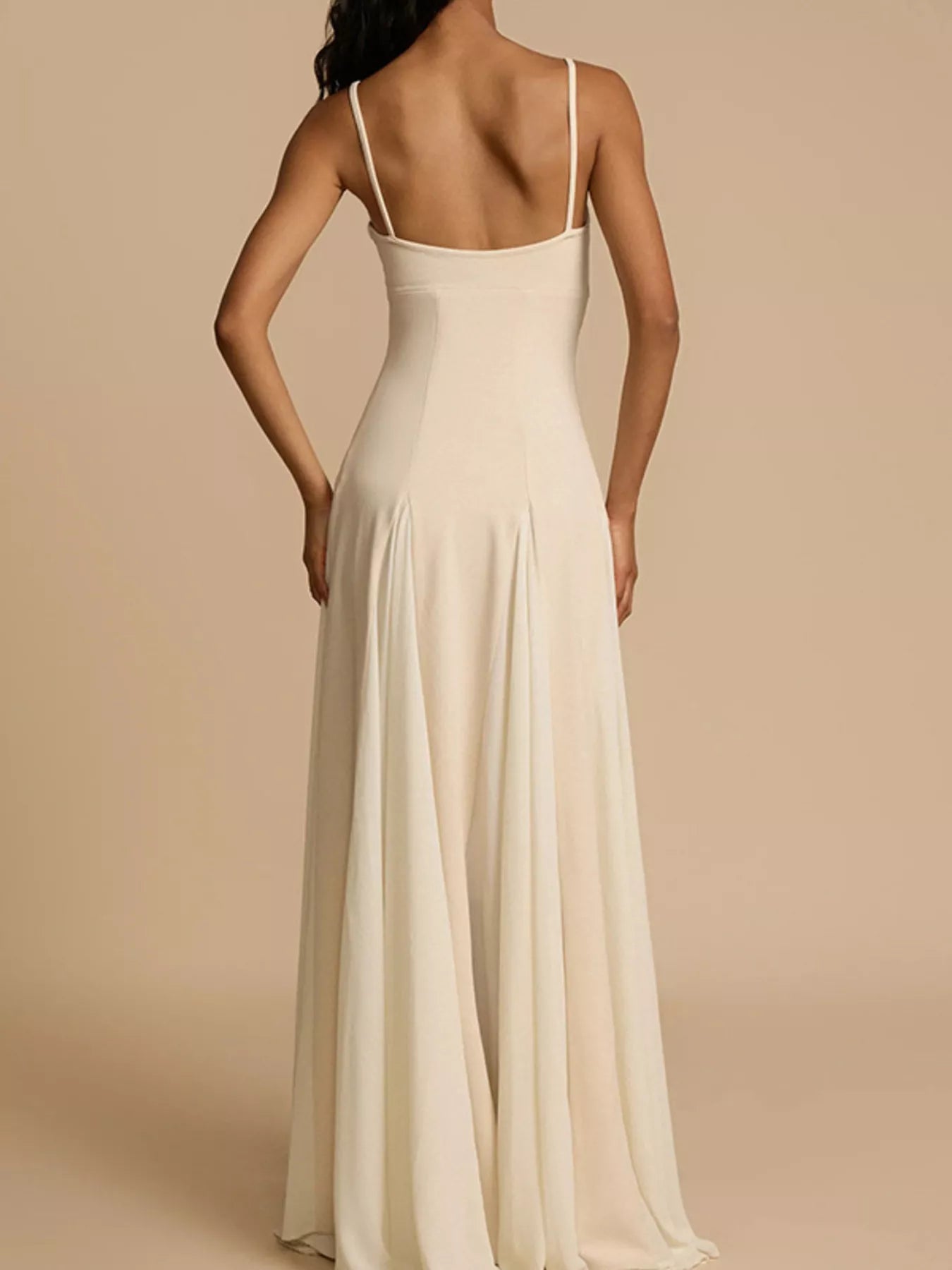 Woman wearing a long, light-colored dress with thin straps on a beige background