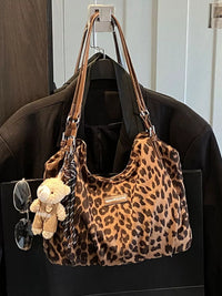 Leopard print handbag with sunglasses and a teddy bear attached, hanging on a coat rack.