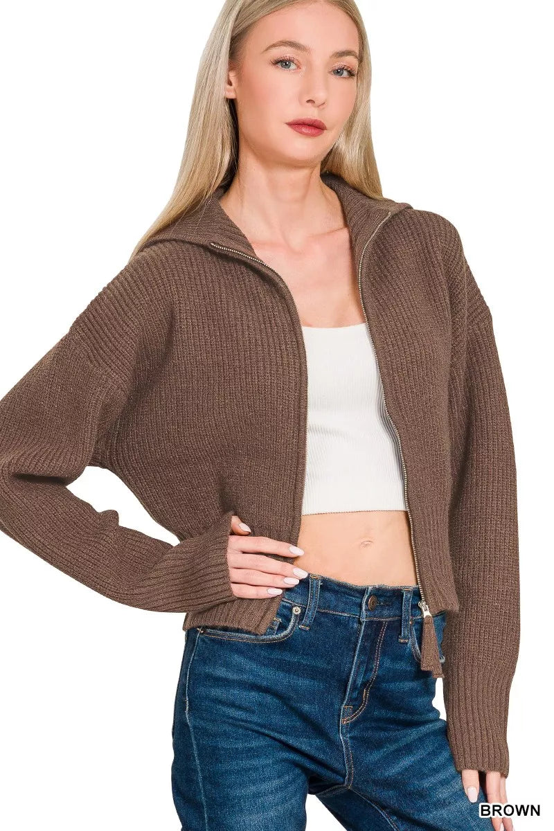 Woman wearing a brown knitted cardigan over a white top and blue jeans on a white background