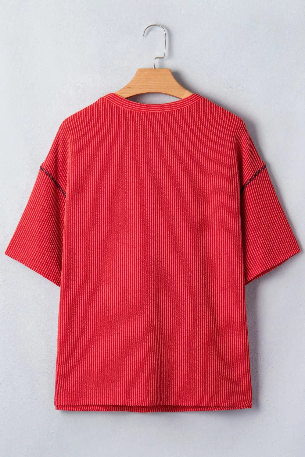 Red ribbed sweater on a wooden hanger against a light gray background