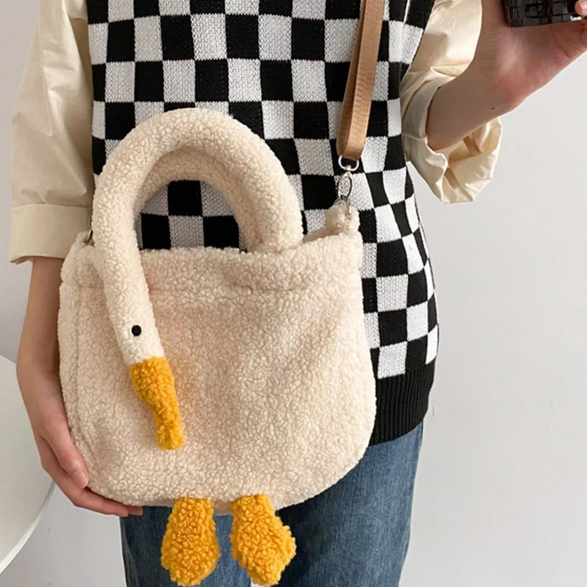 Person holding a fluffy goose-shaped handbag with a checkered background
