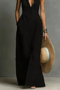 Person wearing a black sleeveless jumpsuit holding a straw hat against a gray background