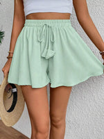 Person wearing light green shorts with a white top against a textured wall.