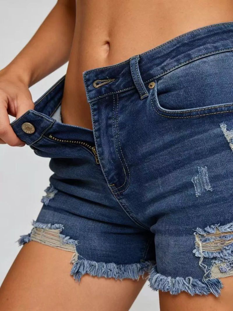 Close-up of a person wearing distressed denim shorts on a plain background