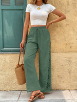 Woman wearing a white crop top and green wide-leg pants, standing against a beige wall.