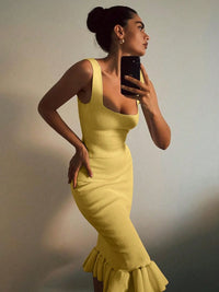 Woman in a yellow dress taking a mirror selfie against a neutral background