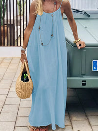 Woman in a long light blue dress holding a woven bag, standing next to a vehicle.