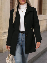 Woman wearing a black coat, white turtleneck, and blue jeans with a neutral background
