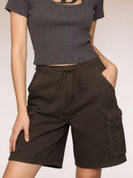 Person wearing a ribbed black crop top and dark brown cargo shorts on a plain background