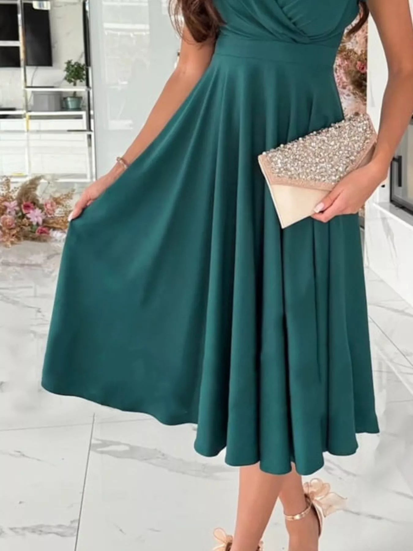 Woman wearing a green dress holding a beige clutch in an indoor setting.