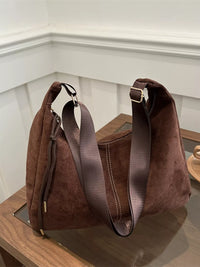 Brown suede handbag with a strap on a wooden surface