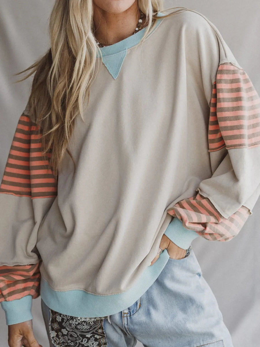 Person wearing a beige sweater with striped sleeves and light blue jeans on a plain background