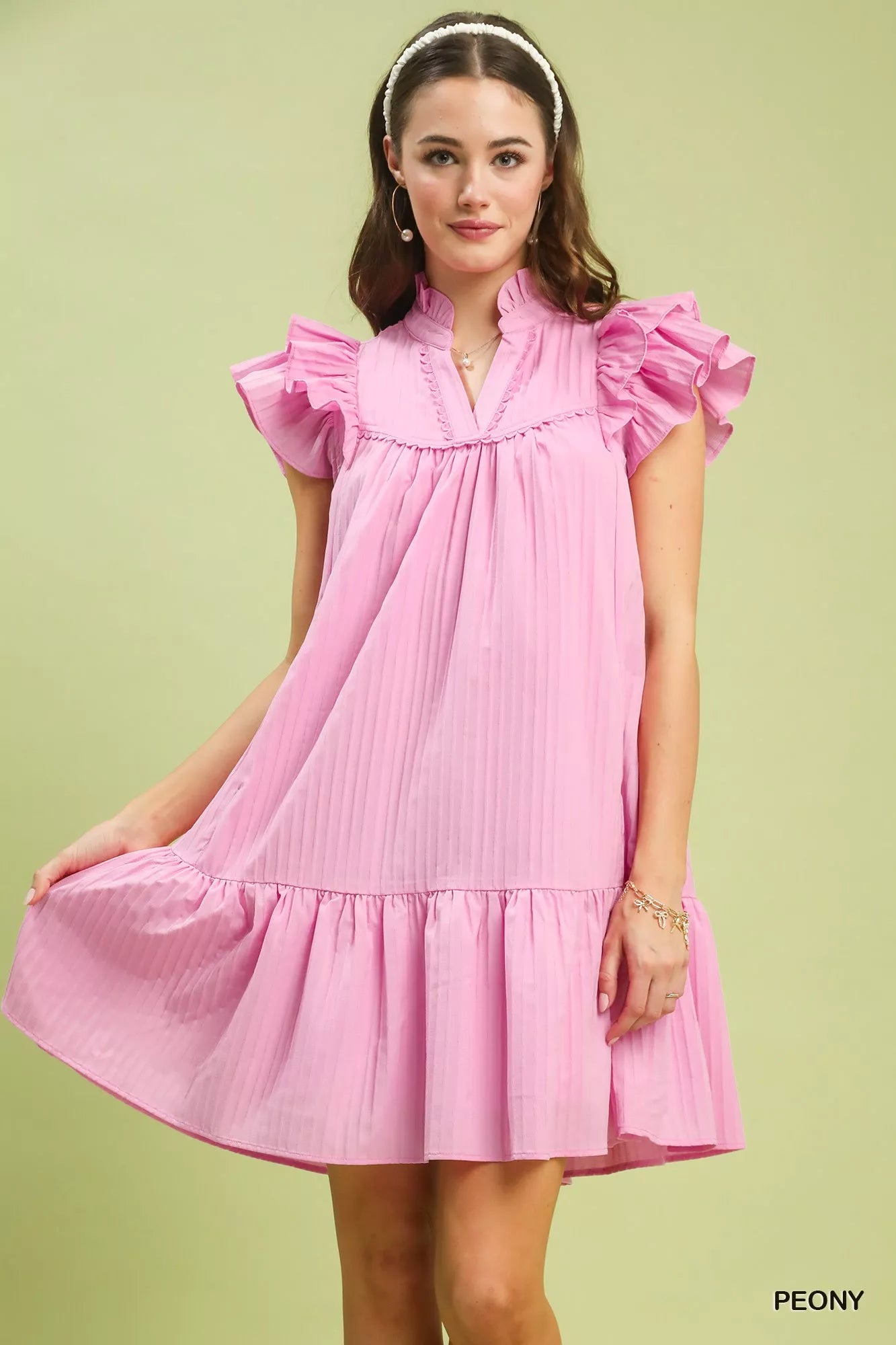 Woman wearing a pink dress with ruffled sleeves on a light green background