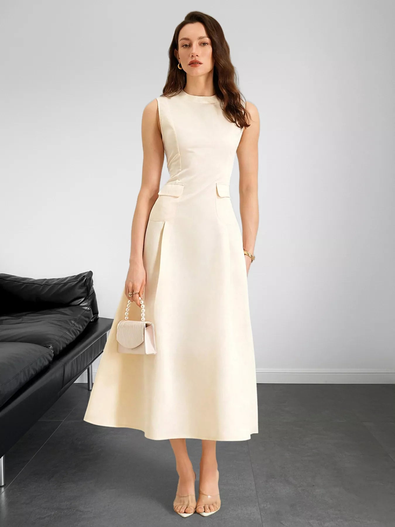 Woman wearing a beige dress standing in a minimalistic room with a black sofa.