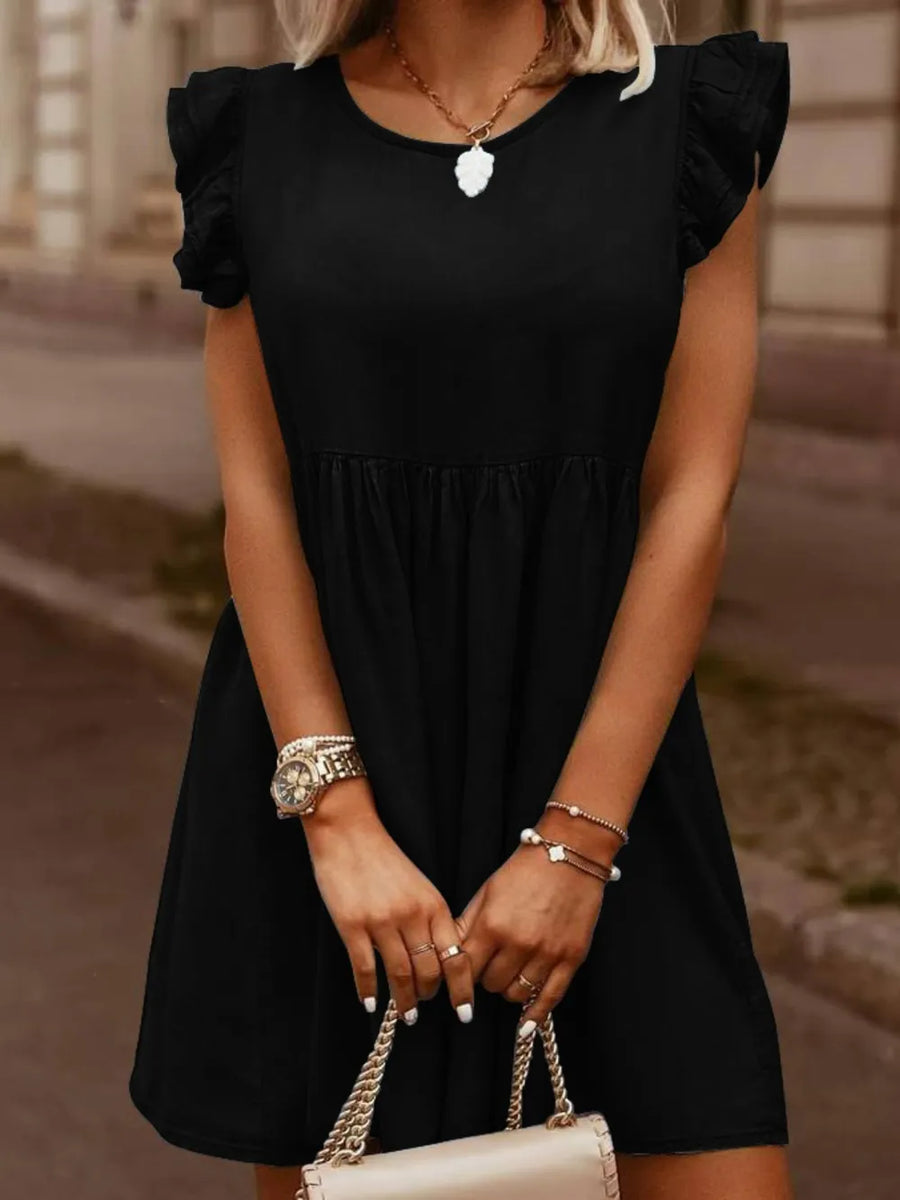 Woman wearing a black dress with ruffled sleeves, holding a cream handbag.