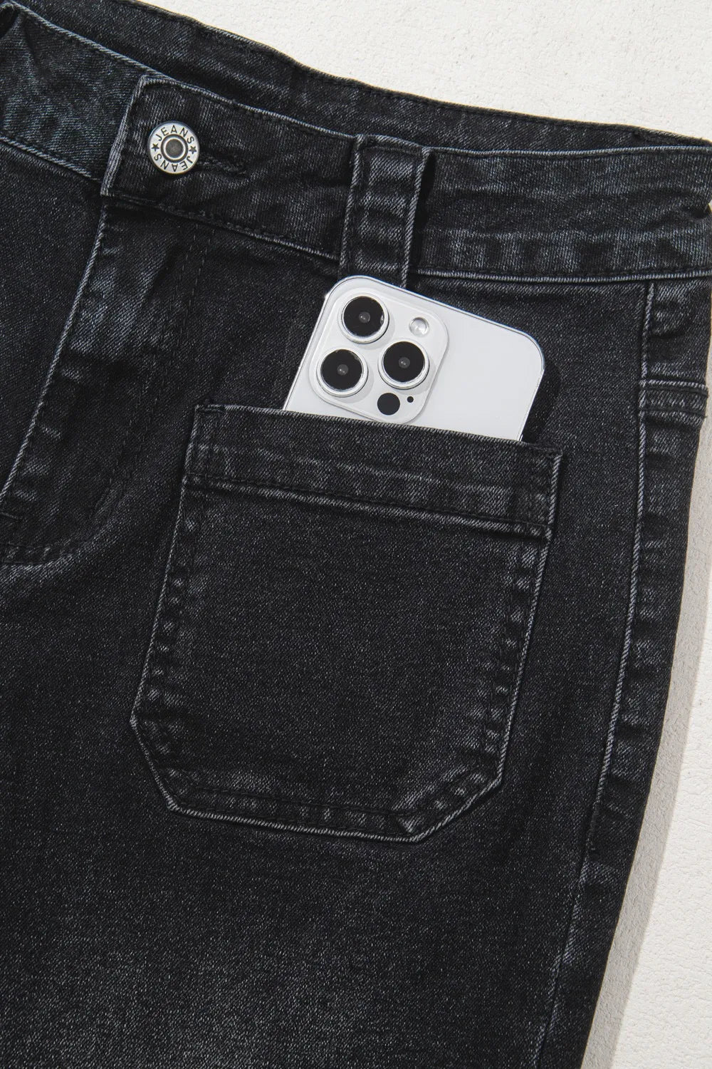 Black denim pocket with a smartphone inside on a light gray background