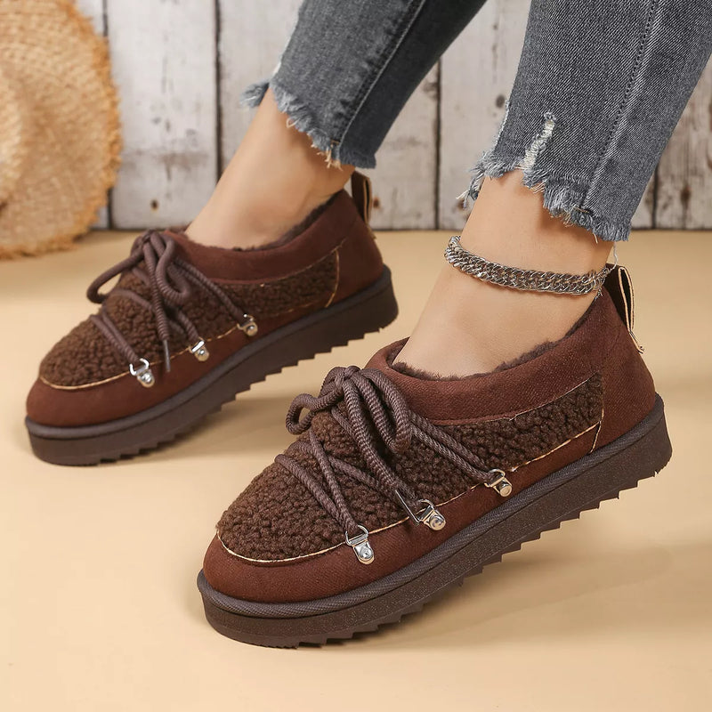 Brown fleece-lined shoes worn with jeans on a wooden floor.