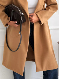 Person wearing a brown coat holding a black bag against a white background