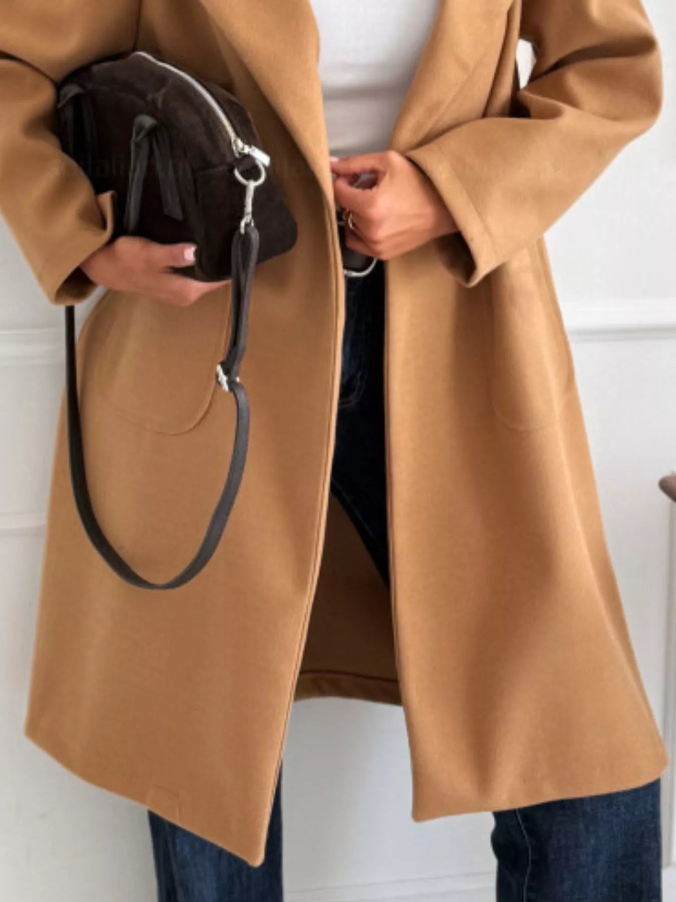 Person wearing a brown coat holding a black bag against a white background