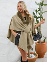Woman wearing a beige poncho with fur trim, standing next to potted plants.