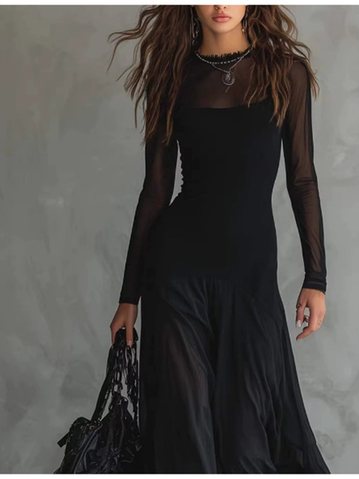 Woman wearing a black dress with sheer sleeves against a gray background