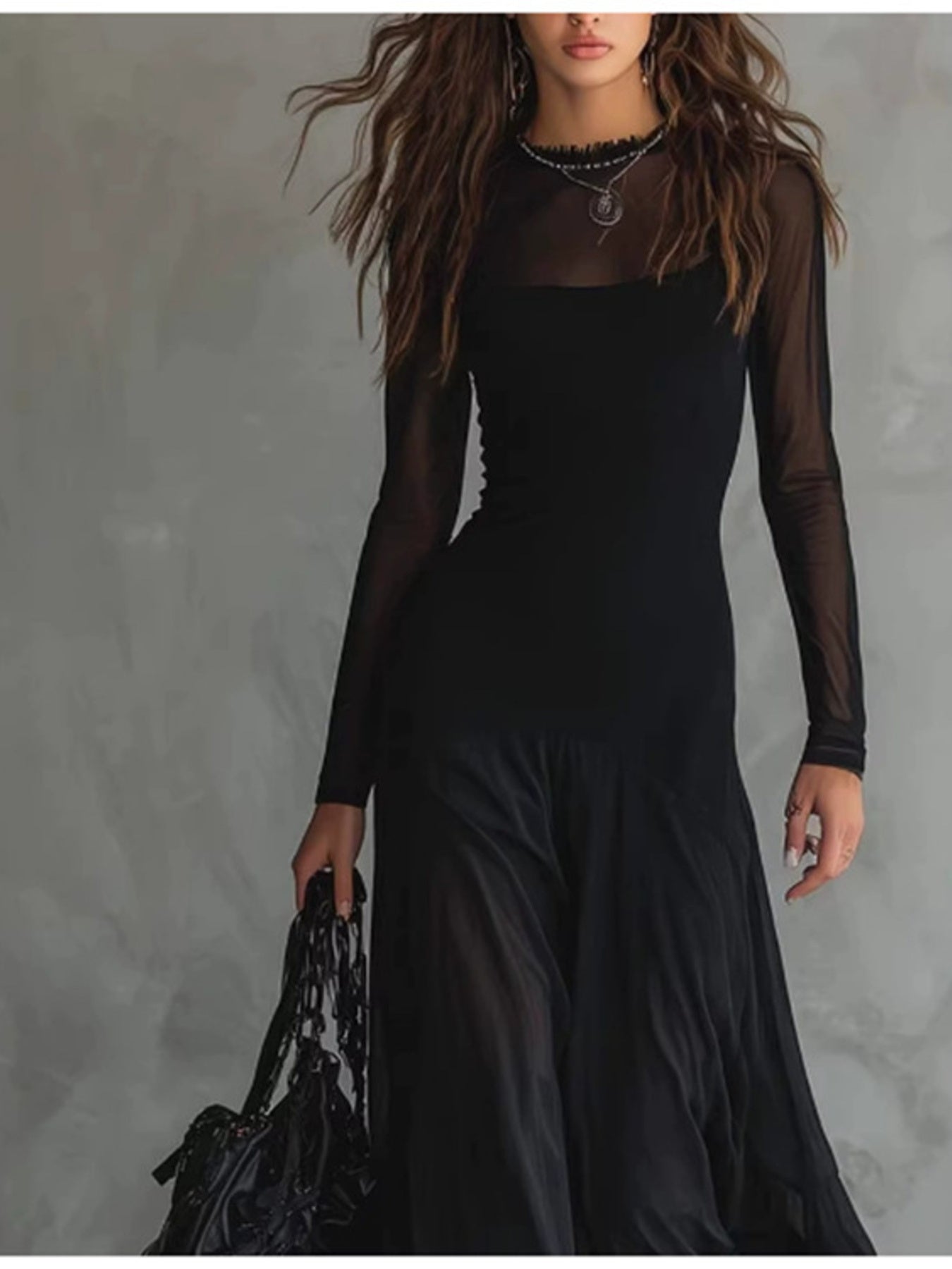 Woman wearing a black dress with sheer sleeves against a gray background