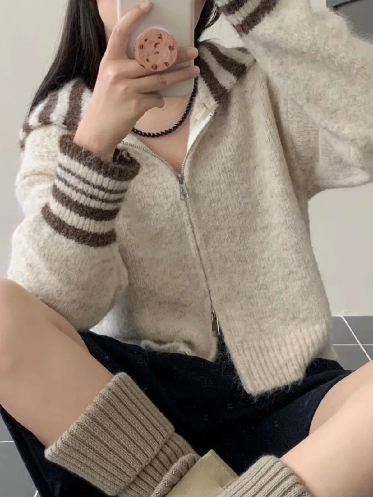 Person wearing a beige and brown striped sweater taking a mirror selfie.