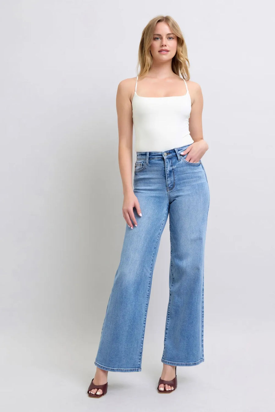 Woman wearing a white top and blue jeans on a plain background