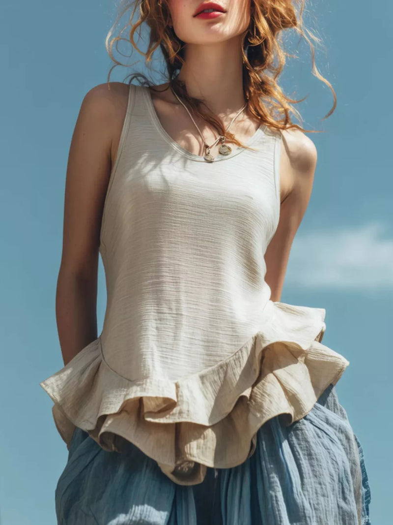 Woman wearing a white sleeveless top with ruffled layers against a blue sky.