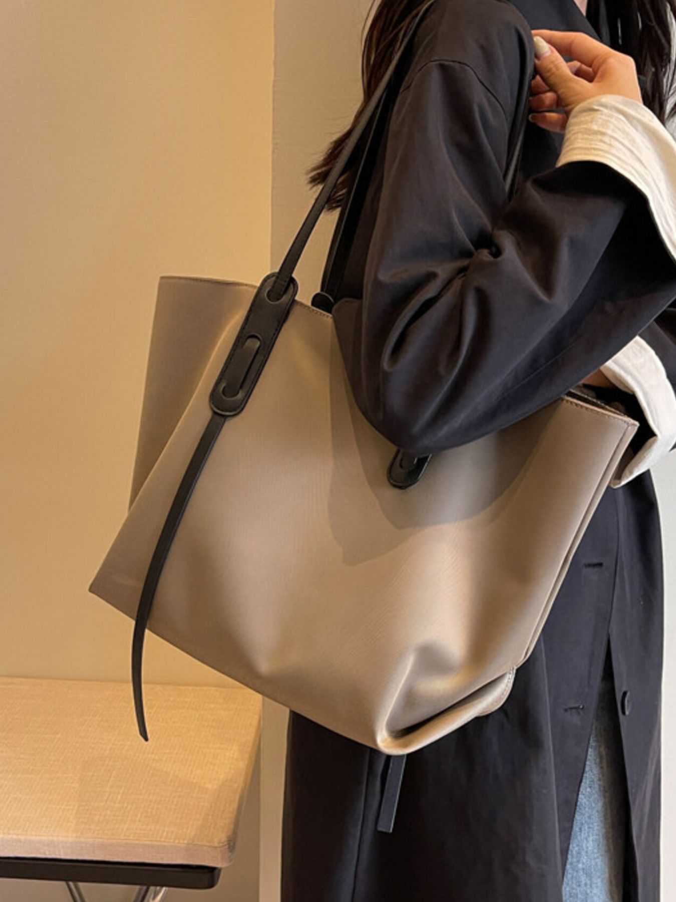 Person holding a beige tote bag with a black handle against a neutral background
