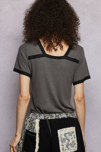 Person wearing a gray textured top with black lace trim against a plain background