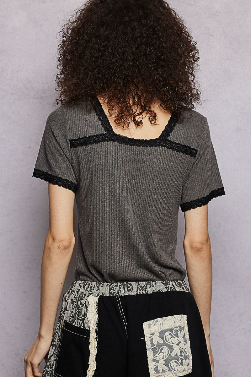 Person wearing a gray textured top with black lace trim against a plain background