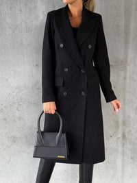 Person wearing a black coat holding a matching black handbag against a gray background