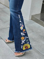 Flared jeans with floral embroidery on a gray pavement background