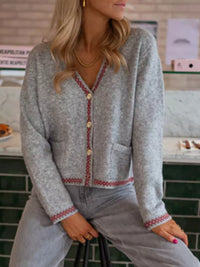 Person wearing a gray cardigan with red trim sitting indoors.
