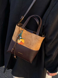 Brown and black handbag with a decorative charm on a dark background