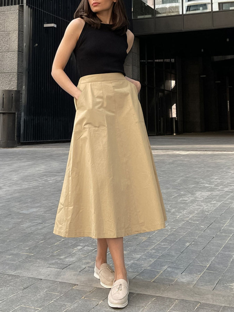 Woman wearing a black top and beige skirt standing on a paved street.