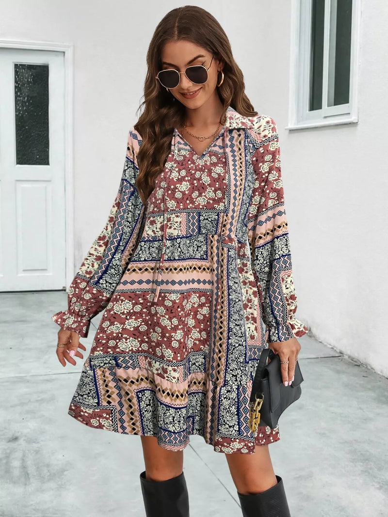 Woman wearing a patterned dress with long sleeves in front of a white wall.